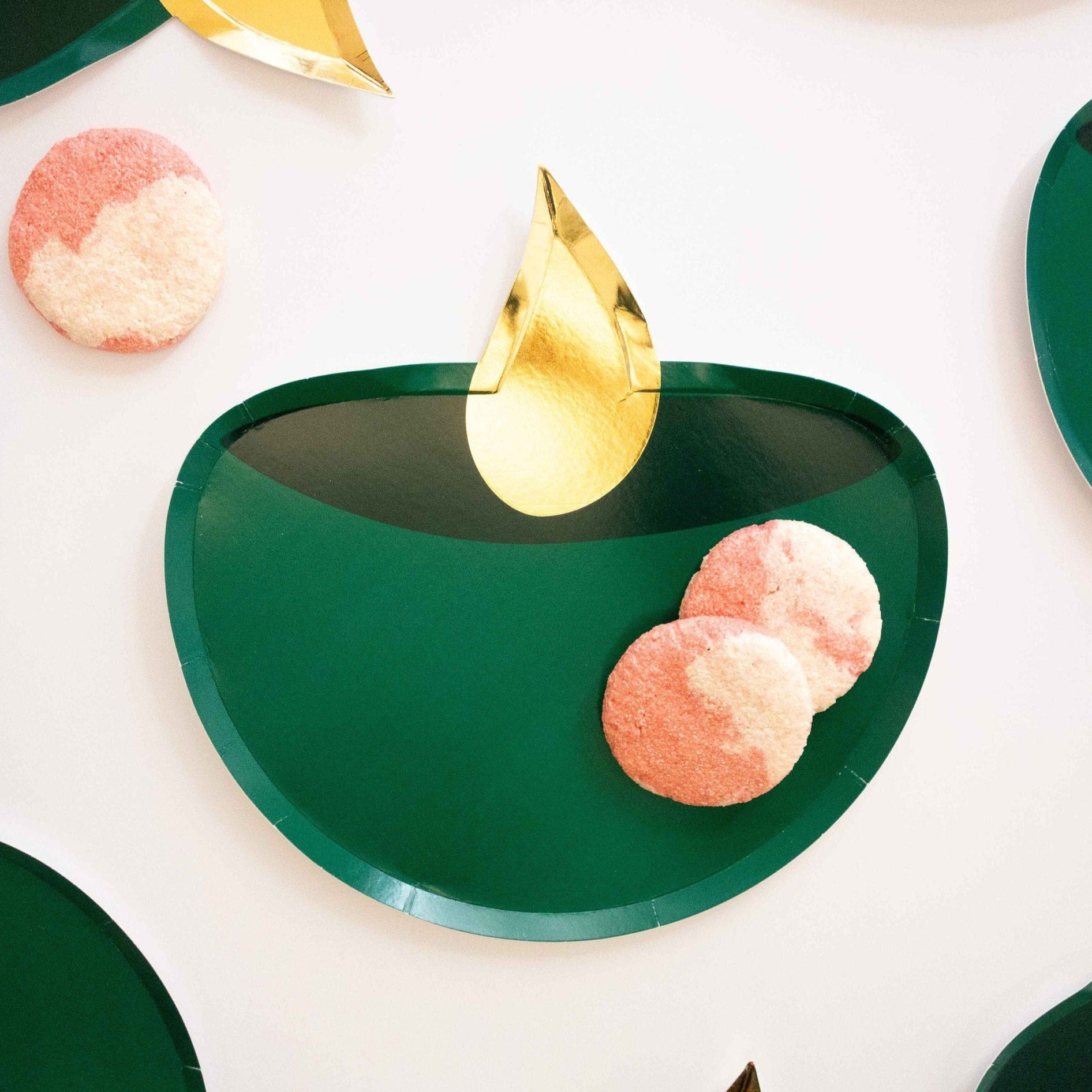 Gold foil and emerald green diya party plate with pink and white cookies on top